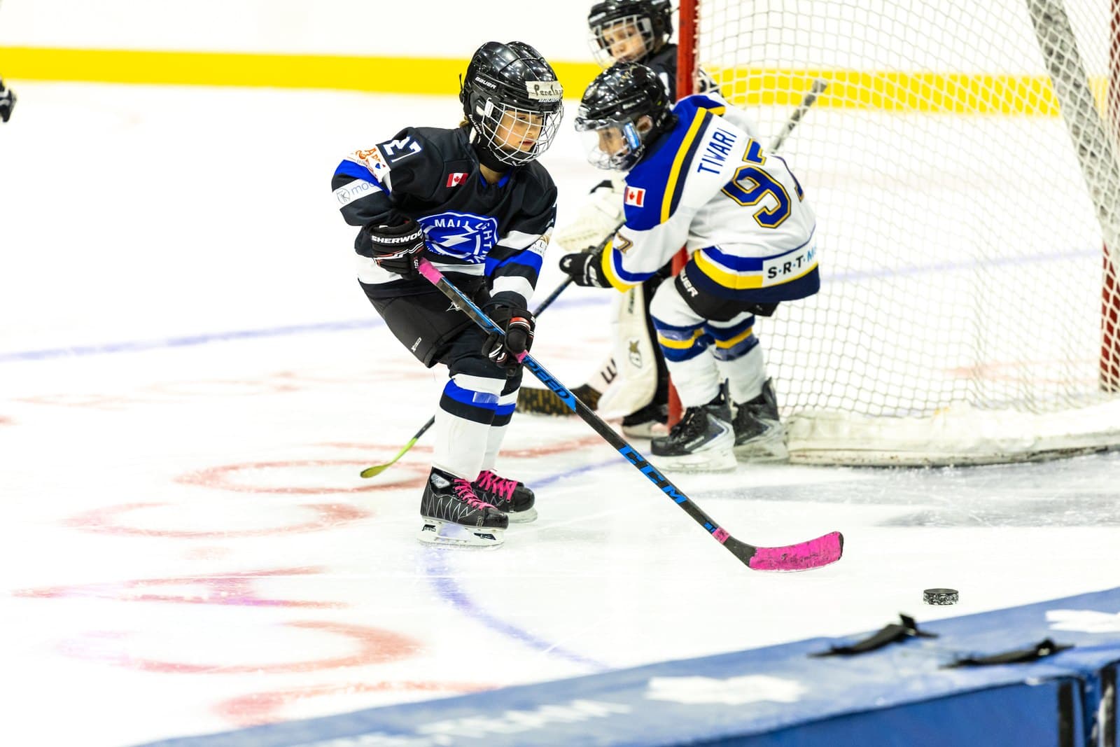 Two skaters lean into each other in a puck battle along the boards